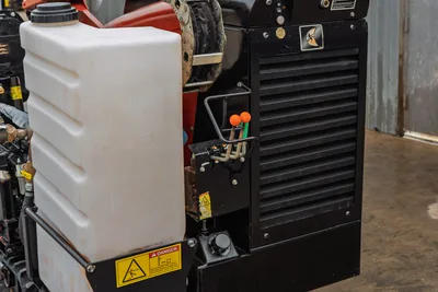 2016 Ditch Witch JT9 engine compartment closeup showing fluid reservoir, louvered cooling panel, hydraulic controls, and danger decals