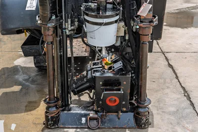 2018 Ditch Witch JT10 drill frame close-up showing vise assembly, hydraulic lines, fluid bucket, and anchor legs from front angle