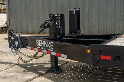 Behnke CBCT2324E-BT-R trailer tongue detail showing gooseneck coupler, safety chains, jack stand, and reflective tape striping