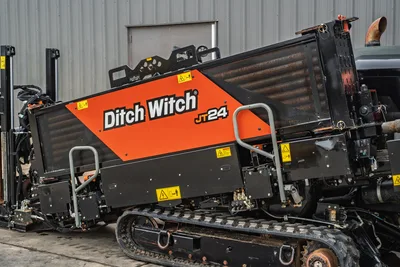 2024 Ditch Witch JT24 HDD drill, close-up side view showing orange engine enclosure, mesh cooling panel, rubber tracks, and hydraulic components.
