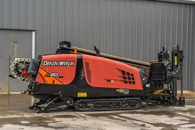 Profile view of 2018 Ditch Witch JT20 HDD drill with rubber tracks, engine compartment, open operator seat, and drill pipe.