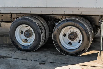 Side view of dual rear wheels and chassis on a 2000 Freightliner FL80 mud truck with white steel rims and used tires.