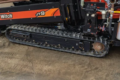 2016 Ditch Witch JT9 rubber track undercarriage close-up showing drive sprocket, track pads, hydraulic lines, and JT9 branding