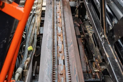 2021 Ditch Witch JT40 drill frame rack-and-pinion thrust system, close-up showing worn steel rack teeth, hydraulic lines, orange frame rail