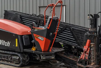 2021 Ditch Witch JT40 HDD drill, side view showing operator platform, red ROPS, drill pipe rack loaded with 3" pipe, rubber tracks