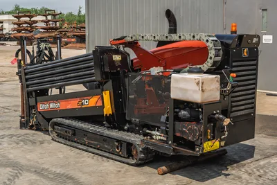 2018 Ditch Witch JT10 HDD drill showing track undercarriage, drill pipe rack, engine compartment, and fluid tank. Rear view.