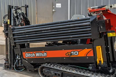 2018 Ditch Witch JT10 HDD drill, side view showing loaded drill pipe rack, rubber tracks, hydraulic components, orange/black bodywork