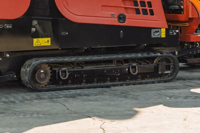 2021 Ditch Witch JT28 rubber track and undercarriage close-up, drive sprocket, safety decals on red lower body panel
