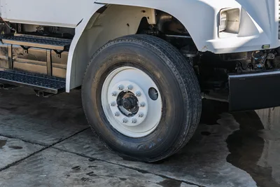Close-up side view of 2000 Freightliner FL80 mud truck front tire, wheel assembly, and black side step.