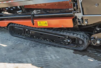 Close-up side profile of 2023 Ditch Witch JT20 rubber track undercarriage and orange safety shielding.