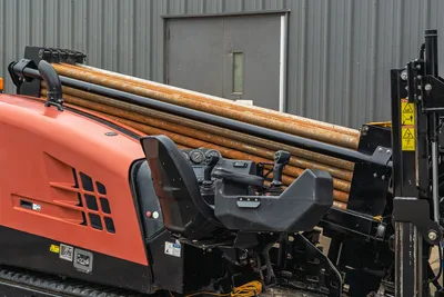 2018 Ditch Witch JT20 operator station, side view showing drill rack, control joysticks, and pipe assembly on tracks.