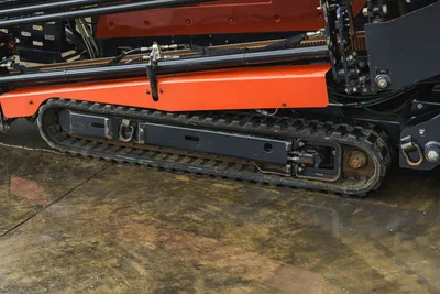 2015 Ditch Witch JT20 rubber track close-up showing undercarriage, drive sprocket, hydraulic lines, and orange frame rail