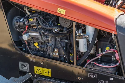 Ditch Witch JT10 engine compartment with 66 hp diesel motor, hydraulic components, fuel filter, battery cables, and safety warning labels visible