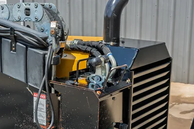 2021 Vermeer D8x12 HDD drill engine compartment closeup showing exhaust stack, hydraulic hoses, louvered cooling panel, and danger decal