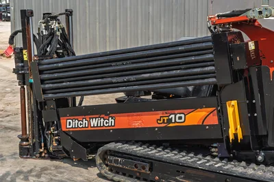 2018 Ditch Witch JT10 HDD drill showing side view of rubber tracks, pipe rack, drill rods, and clean hydraulic components.