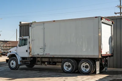 2000 Freightliner FL80 mud truck with white Morgan box body, side view, tandem axle, and rolling rear door.