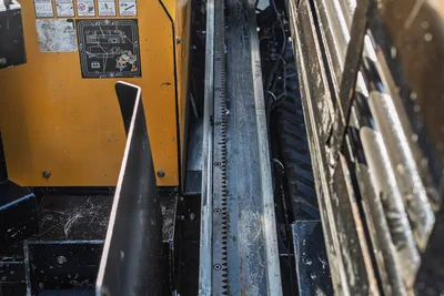 2016 Vermeer D23x30 S3 drill frame rack and pinion thrust chain closeup, yellow chassis panel with safety decals visible