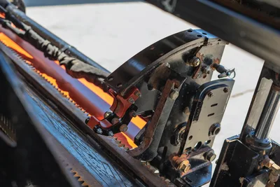 Close-up of Ditch Witch JT20 rack and pinion drill string carriage with pipe loader arm and clamping mechanism.