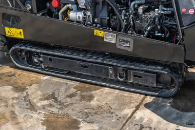 2023 Ditch Witch JT20 rubber track undercarriage close-up showing hydraulic components, safety decals, and tie-down points