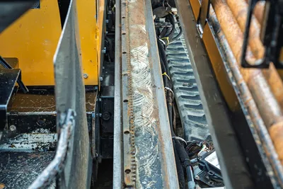 Vermeer D23x30 S3 drill frame rack-and-pinion carriage rail closeup showing wear marks, hydraulic lines, and drill pipe rack