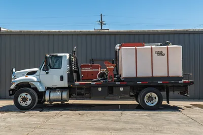 2015 International 7400 mud truck, full driver-side view, flatbed with Ditch Witch FM25 mixer, FM13 pump, and large white poly water tank