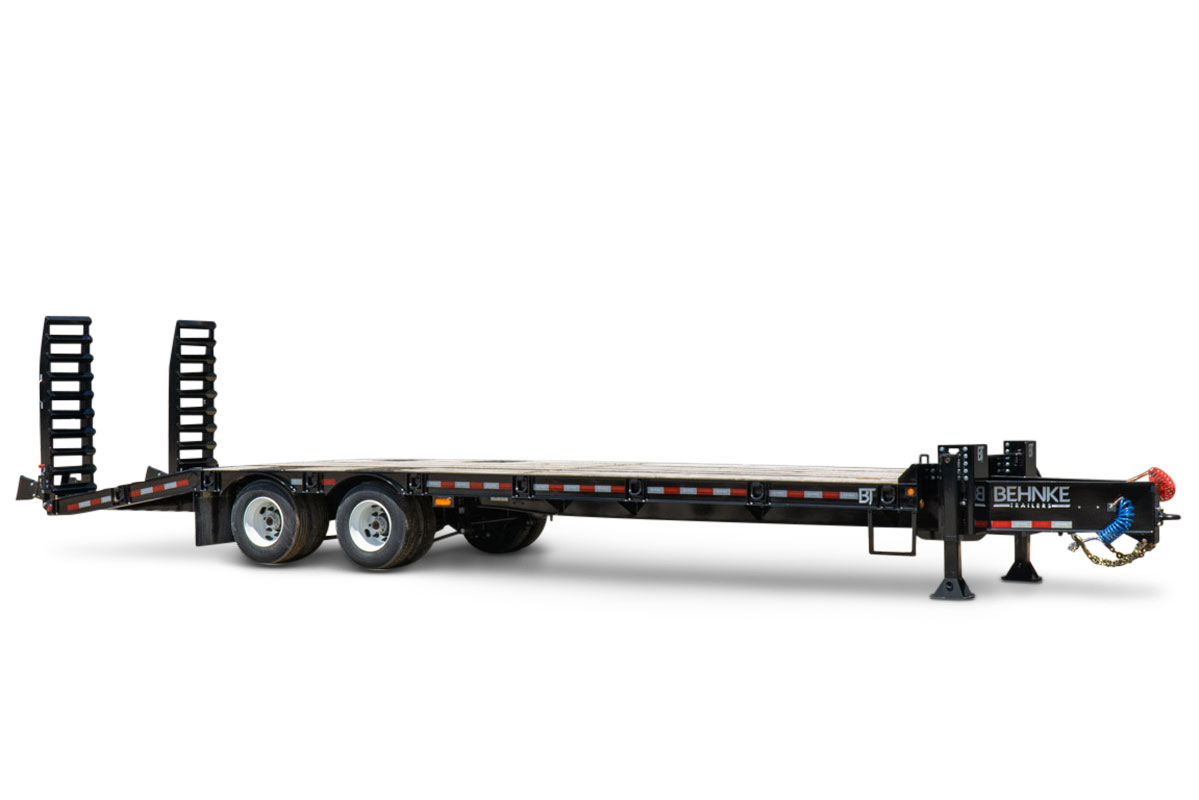 2026 Behnke FB8X30SDPT-40L flatbed equipment trailer, black steel deck, dual tandem axles, fold-up ramps, pintle hitch, side-angle view