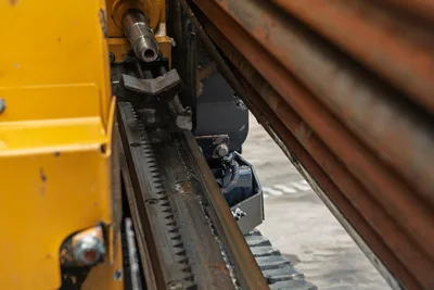 2018 Vermeer D8x12 drill frame closeup showing rack-and-pinion thrust system, vise jaws, hydraulic components, and stacked drill pipe