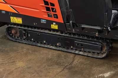 2016 Ditch Witch JT9 rubber track close-up, side view showing wear, drive sprocket, safety decals, and operator seat base