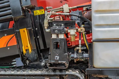 2018 Ditch Witch JT10 hydraulic system close-up showing fluid lines, fittings, mud pump assembly, warning label, and rubber track