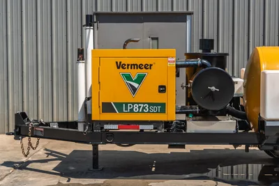 Vermeer LP873SDT vacuum excavator trailer, close-up of yellow engine enclosure with model badging, blower assembly, exhaust stack, tongue with safety chains