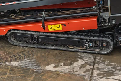 Ditch Witch JT20 tracked undercarriage with orange thrust frame, drill pipe storage, and safety warning label
