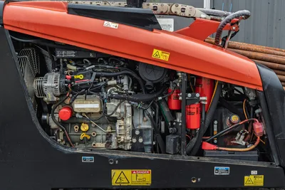 2016 Ditch Witch JT9 open engine compartment showing diesel engine, alternator, hydraulic filters, and wiring harness; drill pipe visible rear