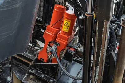 Ditch Witch JT24 rotary drive head with orange power unit, hydraulic hoses, and warning label visible from above