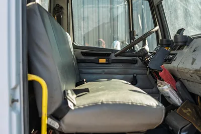 Interior view of 2000 Freightliner FL80 mud truck showcasing worn gray bench seat, steering wheel, and dashboard console.