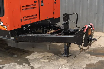 Ditch Witch HX75 trailer tongue with drop-leg jack, pintle hitch, safety chain, and red clevis hook; orange engine enclosure visible