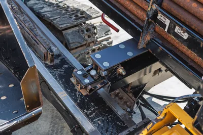2020 Vermeer D24x40 S3 drill frame close-up showing vise block assembly, wear-used steel chassis, rubber tracks, and stacked drill pipe