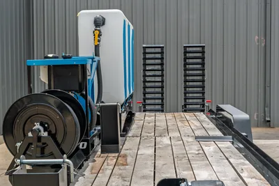 Behnke CBCT2324E-BT-R HDD combo trailer deck with hose reel, white poly tank, blue frame, and stacked pipe racks