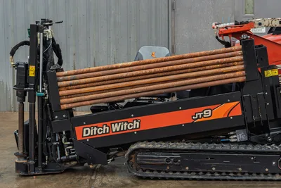2016 Ditch Witch JT9 HDD drill side view showing loaded drill pipe rack, rubber tracks, hydraulic carriage, and operator seat