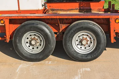 Belshe WB14-2EP trailer tandem axles, Roadmax/Freedom Hauler tires, orange frame, concrete surface, from side.