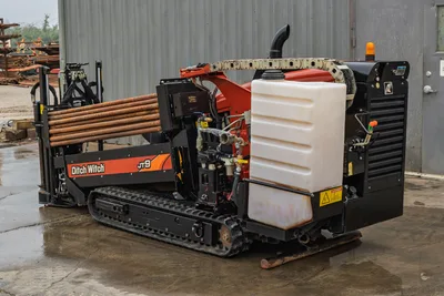 2016 Ditch Witch JT9 HDD drill, rear 3/4 view showing drill pipe rack, fluid tank, engine compartment, rubber tracks, and hydraulic lines.
