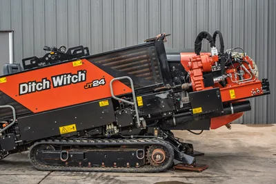 2024 Ditch Witch JT24 HDD drill, close-up side view showing carriage, rotary drive, hydraulic lines, rubber tracks, and engine compartment.
