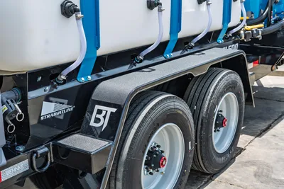Behnke TBCT2220ET-BT-R trailer tandem axle close-up showing dual tires, fender, Straightline/BT logos, white poly tanks, blue frame, fluid hose fittings.