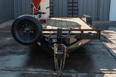 2023 MAXX-D C6X equipment trailer front view showing coupler, safety chains, spare tire, wood deck, and mud mixing equipment loaded on deck