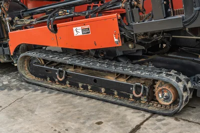 Side profile of Ditch Witch JT3020 MACH 1 showing rubber track undercarriage, drive sprocket, and orange engine cowling.