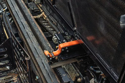 Ditch Witch JT24 drill frame rack-and-pinion thrust system, orange carriage clamp, hydraulic lines, mesh guard panel, overhead angle