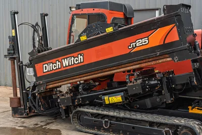 2016 Ditch Witch JT25 HDD drill, close-up of thrust frame, drill pipe, carriage, rubber tracks, and enclosed cab visible