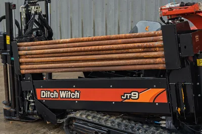 2016 Ditch Witch JT9 HDD drill side view showing loaded drill pipe rack, rubber tracks, operator seat, and hydraulic components