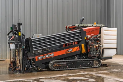 2018 Ditch Witch JT10 HDD drill, side profile view showing rubber tracks, pipe rack with drill pipe, and fluid tank.
