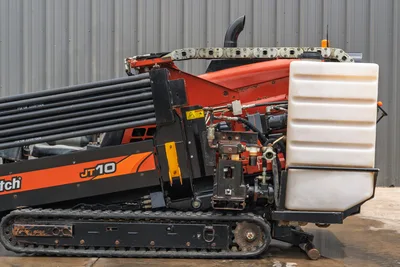 2018 Ditch Witch JT10 HDD drill, side profile showing drill pipe rack, white fluid tank, carriage, and rubber track system.