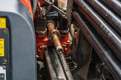Close-up of Ditch Witch JT10 spindle, drill pipe rack, and drive assembly with hydraulic components and rack gear.
